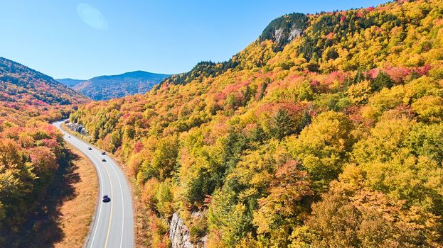 Image of Aerial view of road tucked into New Hampshire mountains covered in peak fall foliage