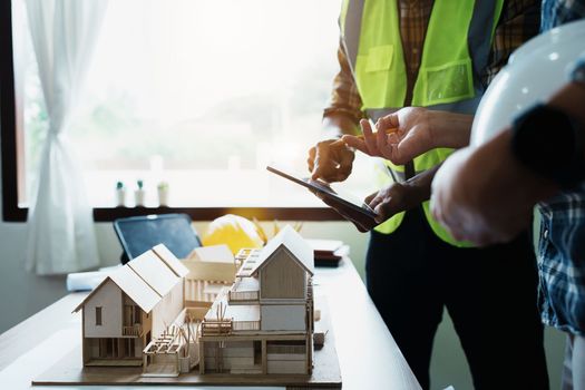 Engineers are consulting the team to design an architectural structure for clients with blueprints and building models to work at office.