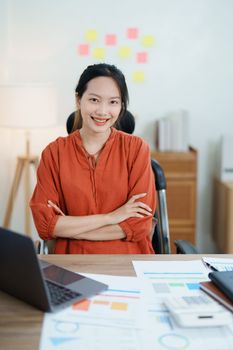 Portrait of a woman business owner showing a happy smiling face as he has successfully invested her business using computers and financial budget documents at work.