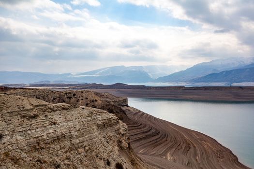 A beautiful reservoir in the mountains. Low water level, drought and beautiful patterns are visible along the banks. A red pleasure boat is standing by the shore