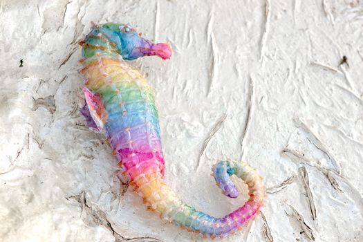 A figurine of a rainbow seahorse, lying on a white textured background. Close up. Copy space