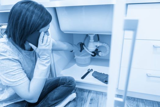 Woman sitting near leaking sink calling for help