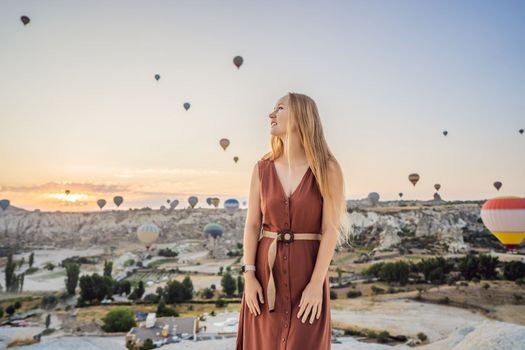 Tourist woman looking at hot air balloons in Cappadocia, Turkey. Happy Travel in Turkey concept. Woman on a mountain top enjoying wonderful view.