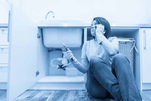 Woman sitting near leaking sink calling for help