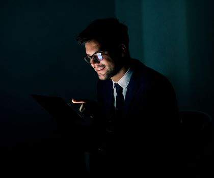 Portrait of a young businessman with tablet or laptop working late at night in office