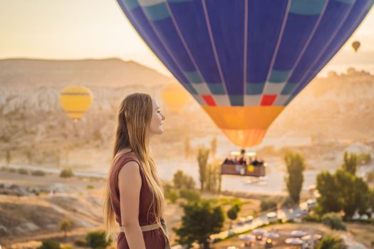 Tourist woman looking at hot air balloons in Cappadocia, Turkey. Happy Travel in Turkey concept. Woman on a mountain top enjoying wonderful view.