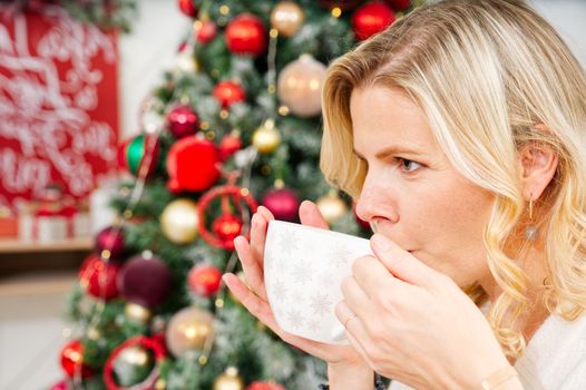 Girl in white sweater holding a cup of warm coffee or tea on background of a Christmas tree. Cozy christmas atmosphere. warming non-alcoholic drink for Christmas. lifestyle