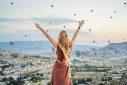 Tourist woman looking at hot air balloons in Cappadocia, Turkey. Happy Travel in Turkey concept. Woman on a mountain top enjoying wonderful view.