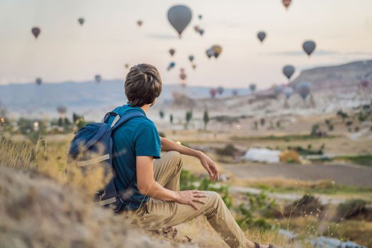 Tourist man looking at hot air balloons in Cappadocia, Turkey. Happy Travel in Turkey concept. Man on a mountain top enjoying wonderful view.
