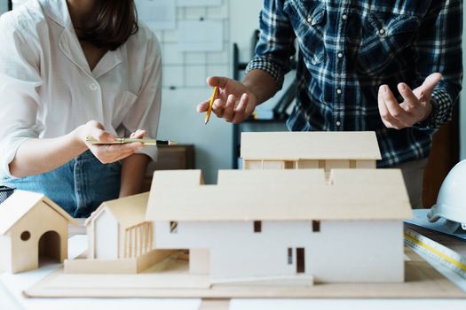 Engineers are consulting the team to design an architectural structure for clients with blueprints and building models to work at office.