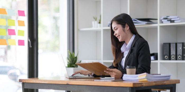 Young asian beautiful and charming busineswoman smiling and working on laptop computer at office...