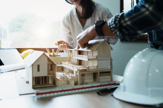 Engineers are consulting the team to design an architectural structure for clients with blueprints and building models to work at office.