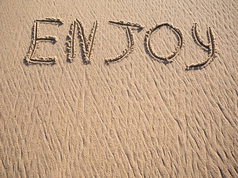 Enjoy word is written on the beach sand with copy space.