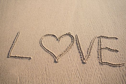 The word LOVE written in the sand on the beach with heart sign and copy space. Love is all you need.