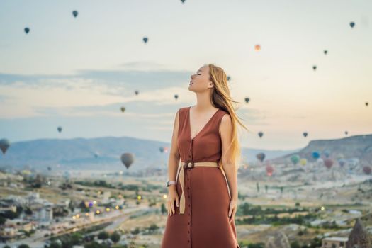 Tourist woman looking at hot air balloons in Cappadocia, Turkey. Happy Travel in Turkey concept. Woman on a mountain top enjoying wonderful view.
