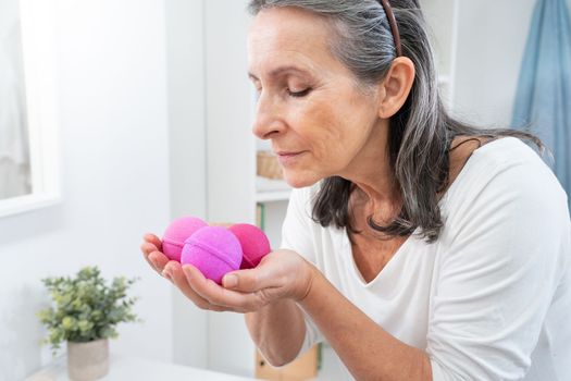 Cosmetic and beauty concept. Middle aged woman smelling aroma soap balls at bathtub. Body and skin care lifestyle.