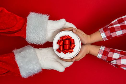 Santa's hands give gifts to children at Christmas. red background with copy space Christmas time