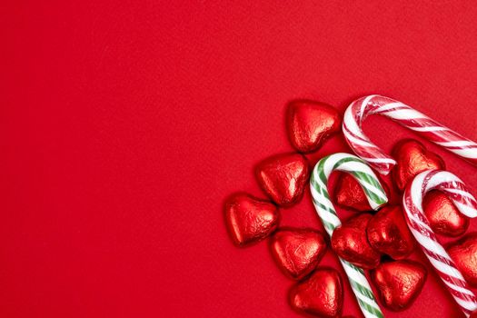 red festive Christmas background with candy in the shape of hearts wrapped in shiny foil and candy in the shape of a caramel cane