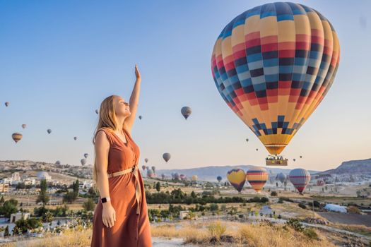Tourist woman looking at hot air balloons in Cappadocia, Turkey. Happy Travel in Turkey concept. Woman on a mountain top enjoying wonderful view.