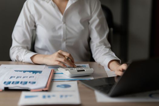 Close up Business woman using calculator and laptop for do math finance on wooden desk in office and business working background, tax, accounting, statistics and analytic research concept.