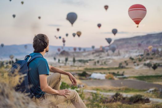 Tourist man looking at hot air balloons in Cappadocia, Turkey. Happy Travel in Turkey concept. Man on a mountain top enjoying wonderful view.