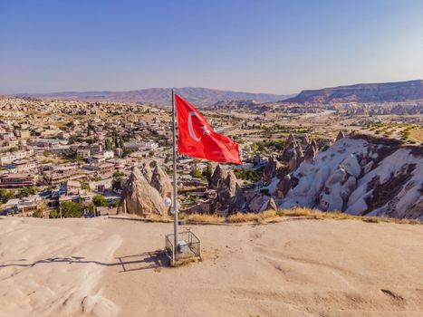 Turkish flag on the hill with typical tuff rock formations of the Cappadocia against the backdrop of a blue sky, Goreme, Turkey.