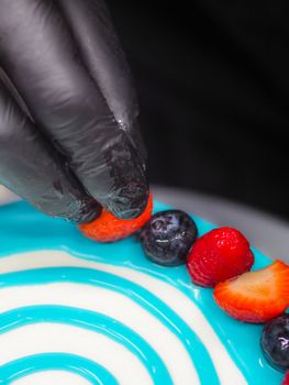 pastry chef cake designer decorating turquoise blue white frosted cheesecake in kitchen with piping bag