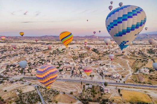 Colorful hot air balloons flying over at fairy chimneys valley in Nevsehir, Goreme, Cappadocia Turkey. Spectacular panoramic drone view of the underground city and ballooning tourism. High quality.