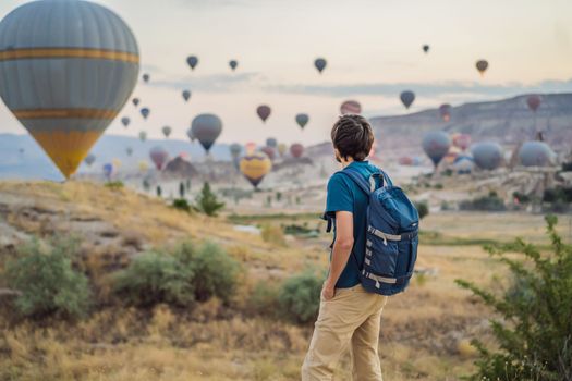 Tourist man looking at hot air balloons in Cappadocia, Turkey. Happy Travel in Turkey concept. Man on a mountain top enjoying wonderful view.