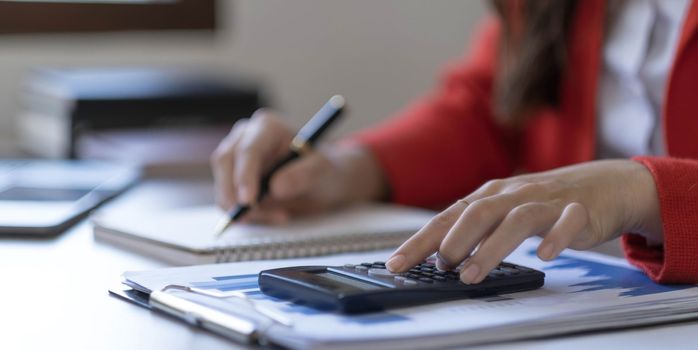 Asian Business woman using calculator and laptop for doing math finance on an office desk, tax, report, accounting, statistics, and analytical research concept..