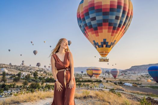 Tourist woman looking at hot air balloons in Cappadocia, Turkey. Happy Travel in Turkey concept. Woman on a mountain top enjoying wonderful view.