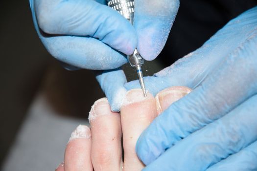 A master in a beauty salon makes a hardware pedicure to a client, Fraser removal of red varnish and cuticles. Close-up, soft focus. High quality photo