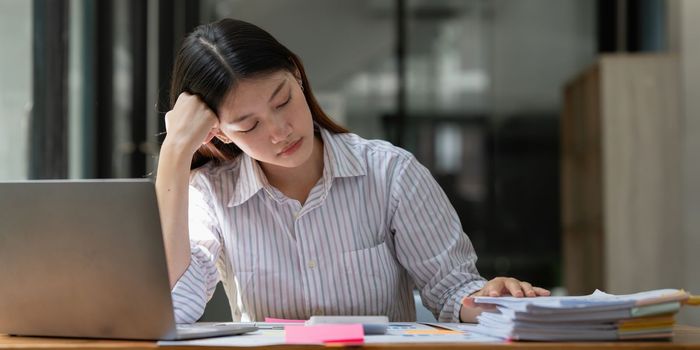 Stressed Asian business woman worry with many document on desk at office.