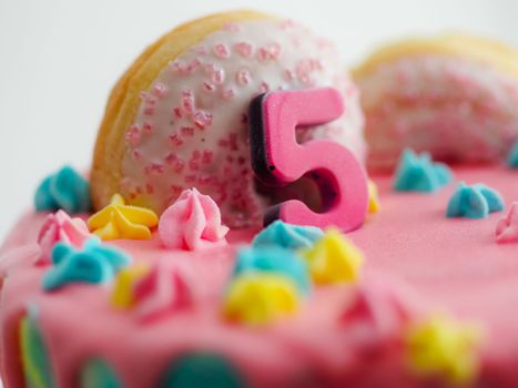 Close up of pink frosted dripping cake with donut and plastel brushed royal star sprinkles insolated on white studio shot