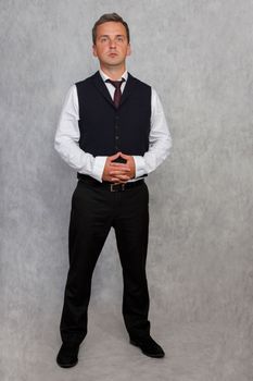 Portrait of a concerned boss. Handsome businessman in a vest and shirt standing with folded hands. Light studio background.