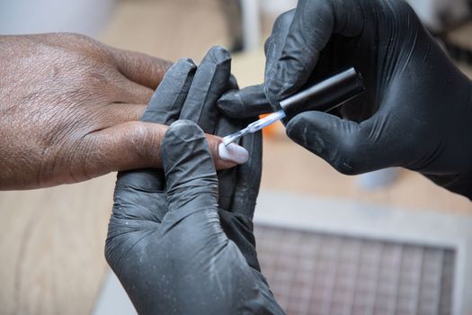 Manicurist covers the nails of a dark-skinned girl with blue gel polish in a beauty salon, High quality photo