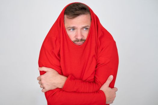 Young caucasian man ihiding pulling sweater on head in displeasure, keeps arms folded. 