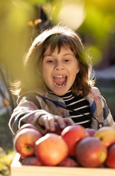 Portrait of healthy girl eating big red apple. Attractive caucasian girl with apple, isolated on green background. Schoolgirl smiling and looking at apples with fresh fruit - emotional portrait.