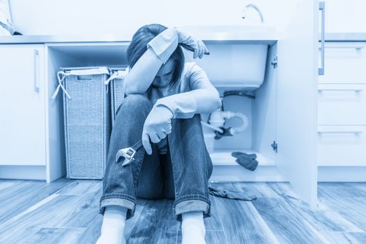 Woman sitting near leaking sink calling for help