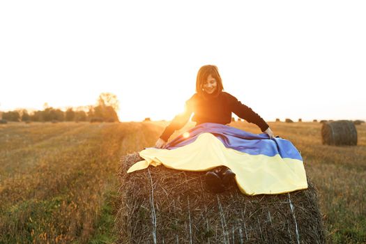 Portrait of little girl holding a yellow and blue flag of Ukraine on a background of sunset sky. Stop war in Ukraine. Russia stop war. Kid outdoors. International day of democracy concept.