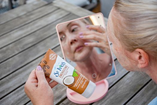 ST. Ives Fresh Energizing Coconut and Coffee Scrub in Tube, reflections in the mirror, a middle-aged woman applies a scrub on her face in front of a mirror, As,Belgium, August 13,2022, High quality photo