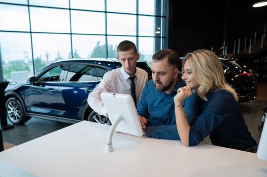 Caucasian married couple chooses a car in a car dealership on digital tablets