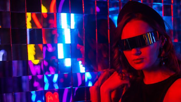 Portrait of a caucasian woman in sunglasses in neon light against a mirror wall