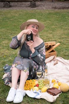 a young woman in a long dress and straw hat is resting on a picnic with fruits, cheese plate and champagne, rest from worries and household chores parks and recreation areas,.High quality photo