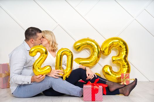 Young couple having romantic date on Christmas eve with 2023 golden foil inflatable balloons. Christmas and 2023 New Year Holidays concept.