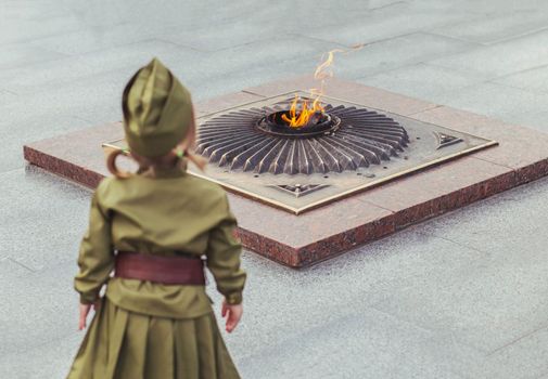 baby in a Soviet military uniform looks at the monument to those killed in World War II