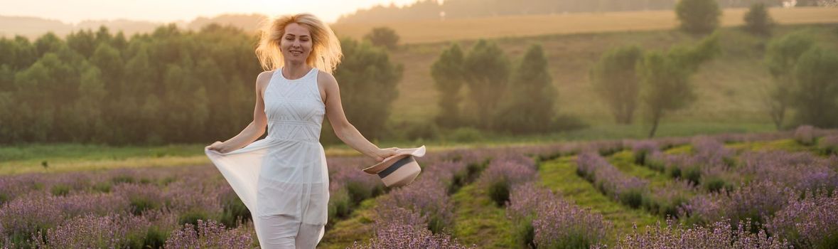 Beautiful young woman wearing a white dress walking in the middle of a lavender field in bloom.