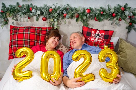 beautiful couple laying in bed, planning to have a baby. Christmas and happy New Year wishes with numbers 2023.