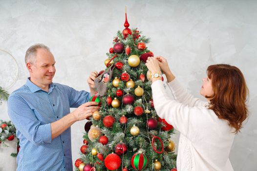 Smiling happy middle age couple decorating christmas tree at home. Happy couple decorating Christmas tree together at home. Happy Family xmas concept