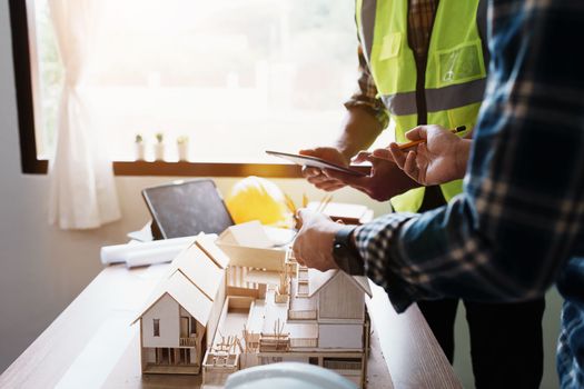 Engineers are consulting the team to design an architectural structure for clients with blueprints and building models to work at office.